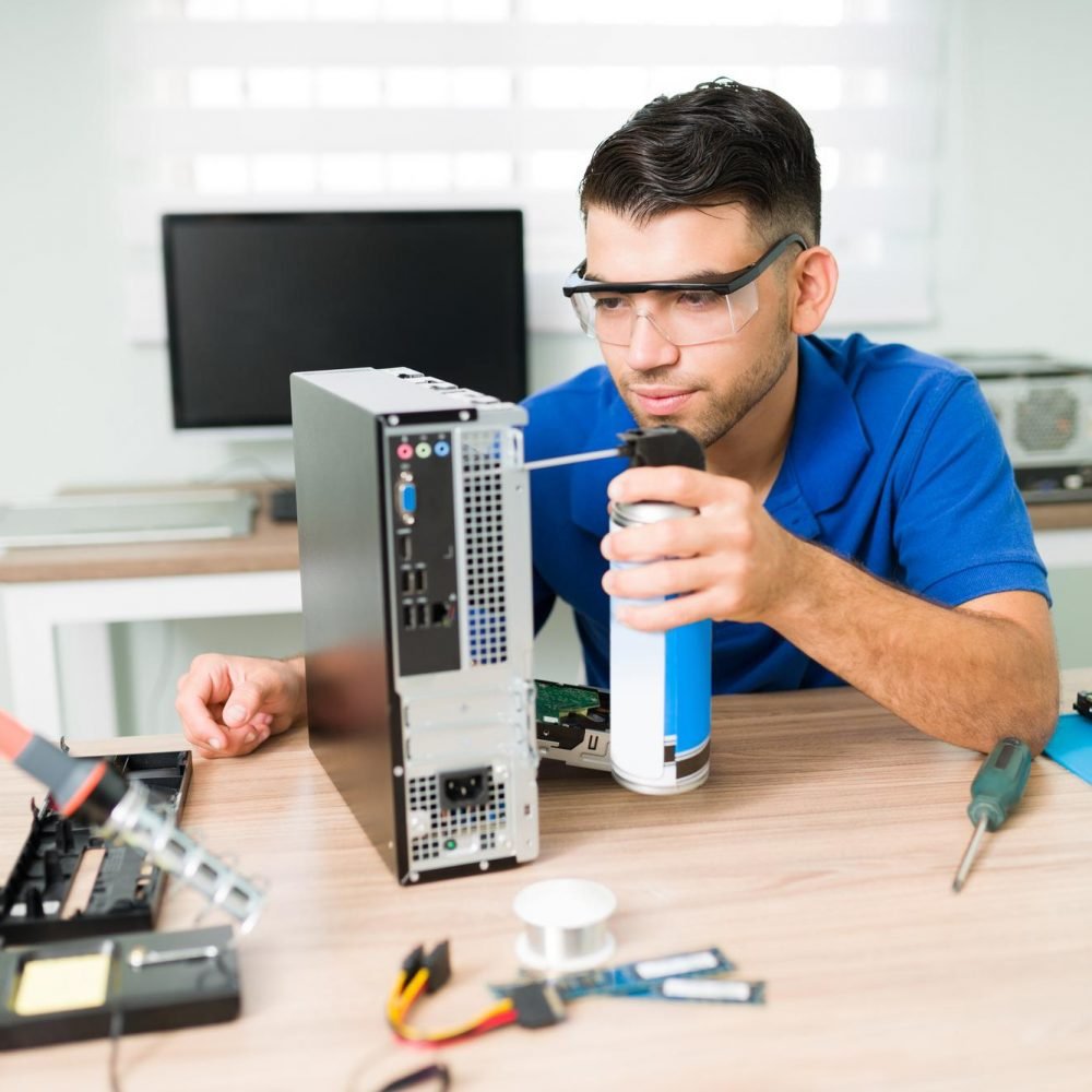 dirty-computer-attractive-young-man-wearing-protection-glasses-while-cleaning-inside-with-compressed-air-the-hardware-of-computer